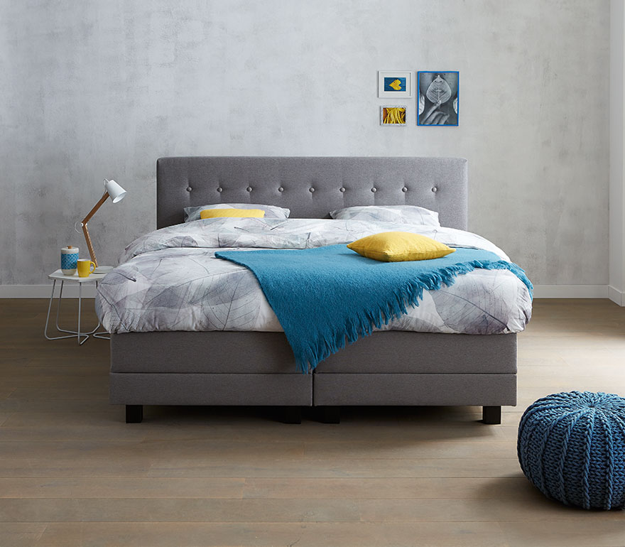 Polypreen boxspring in een slaapkamer met grijze bekleding en blauwe accenten