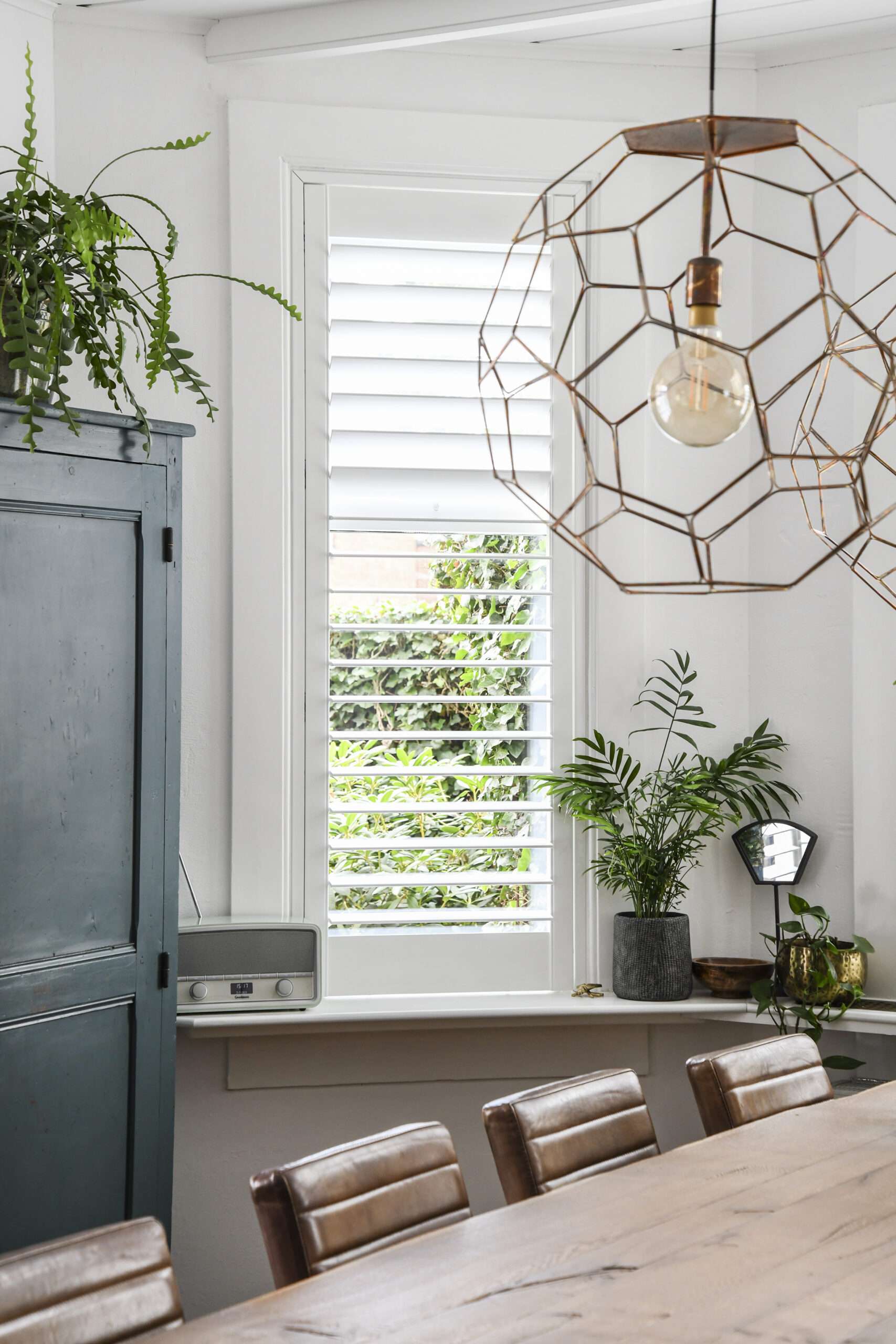 Witte Blend shutters in een eetkamer met groene kast en houten tafel