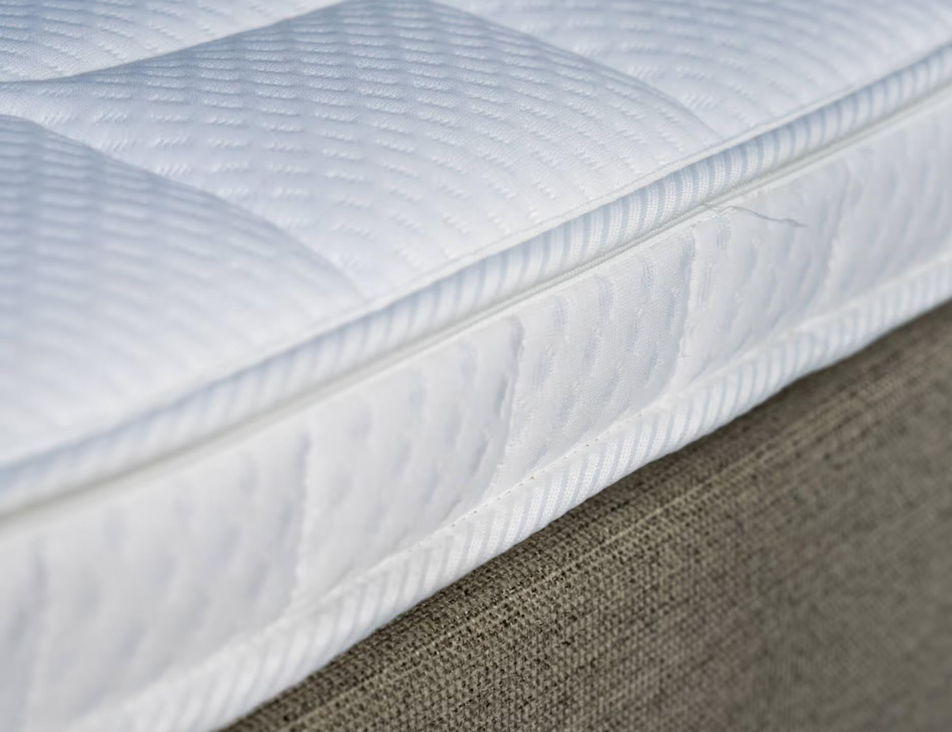 Close-up van de witte doorgestikte Ubica topper op een gestoffeerd bed
